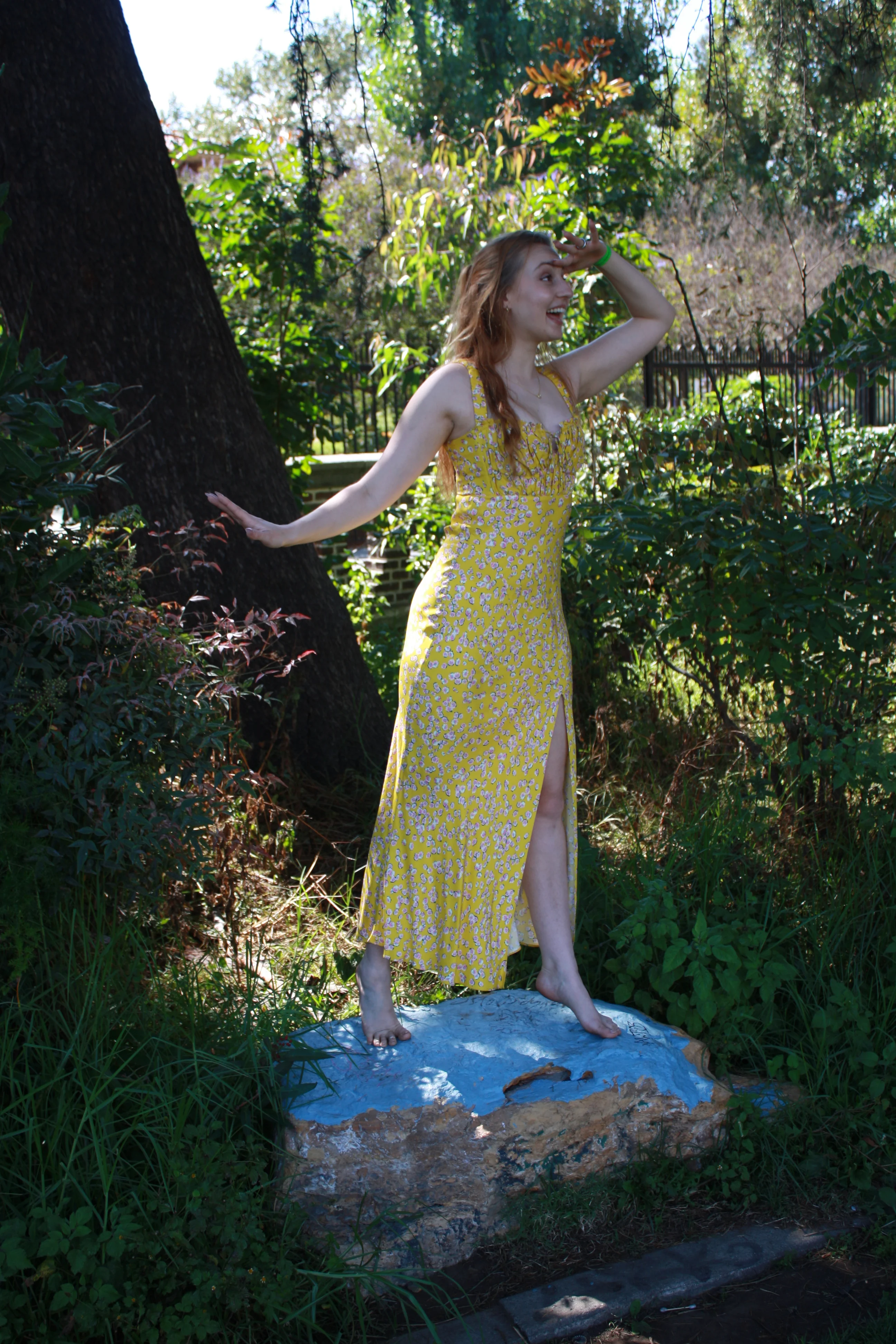 Jordie Morris standing on a blue-painted rock with one arm raised at the Exposition Park Rose Garden.